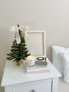 a small christmas tree sitting on top of a white table next to a clock and candle