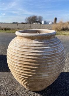 a large vase sitting on top of a road next to a grass and dirt field