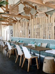 the interior of a restaurant with wooden tables and white chairs, blue upholstered benches and bamboo screens