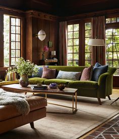 a living room filled with lots of furniture next to large windows and wooden paneled walls