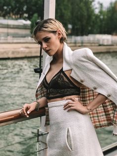 a woman standing on top of a boat next to the water with her hands in her pockets