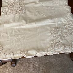 an old white table cloth with embroidered flowers and leaves on it, sitting on the floor