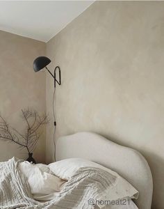 an unmade bed with white linens and a black lamp on the wall above it