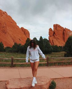 a woman in white shirt and shorts standing on rock