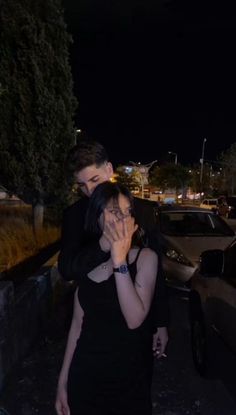 a man and woman standing next to each other in front of a car at night