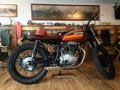 an orange and black motorcycle parked inside of a room next to a wooden table with pictures on the wall