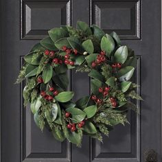 a christmas wreath hanging on the front door with red berries and green leaves around it