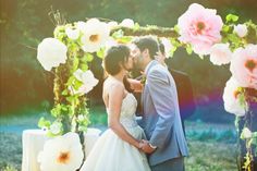 a bride and groom kissing under an arch decorated with flowers