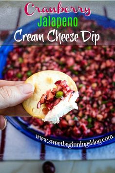 a hand holding a cracker over a bowl of cranberry jalapeno cream cheese dip