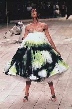 a woman in a green and white dress standing on a wooden floor with her eyes closed