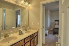 a bathroom with double sinks and large mirror in it's center area, next to a bed