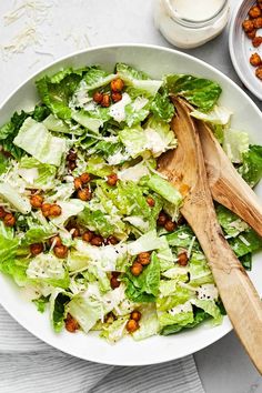 a white bowl filled with lettuce and chickpeas next to a wooden spoon