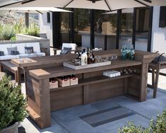 an outdoor bar is set up with bottles and glasses on the table, under an umbrella