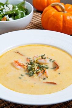 there is a bowl of soup with shrimp and cheese in it next to some pumpkins