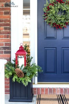 a blue front door with a red lantern and evergreen wreath on it, sitting next to a black potted planter