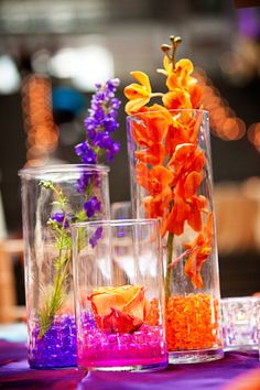 three vases filled with flowers on top of a purple and orange table cloth covered table