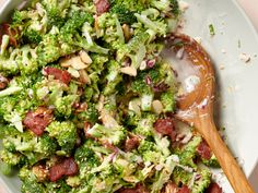 broccoli salad with bacon and onions in a white bowl next to a wooden spoon