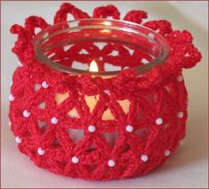 a red crocheted candle holder with a lit candle in the center and white dots on it