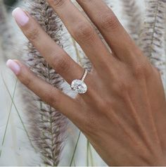 a woman's hand with a diamond ring on top of her finger and grass in the background