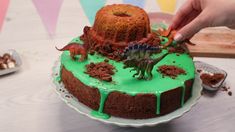 someone is decorating a dinosaur cake with green icing