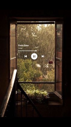 an open window with rain falling down on the ground and plants in front of it