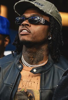 a close up of a person wearing sunglasses and a hat with tattoos on his chest