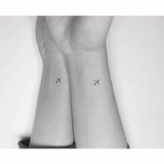 two small tattoos on the wrist that are both black and white, one with an airplane