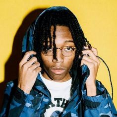 a young man with dreadlocks is holding his hands to his ears and looking at the camera