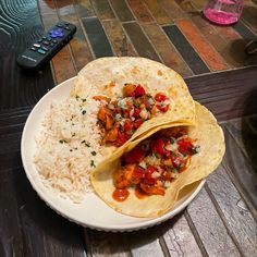 two tortillas on a plate with rice and salsa next to a remote control