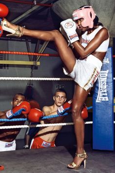 a woman kicking a boxing ball with her leg in the air while two men look on