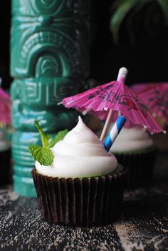 two cupcakes with white frosting and an umbrella on top are sitting next to each other