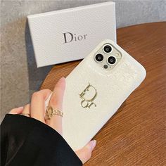 a person holding an iphone in their hand next to a dior phone case on a table