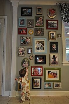 a little boy standing in front of a wall covered with pictures and framed photos on it