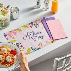 a person holding a plate with waffles on it next to flowers and drinks