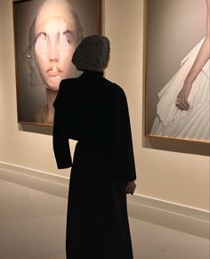 a woman standing in front of two paintings with her head turned to the side and hands behind her back