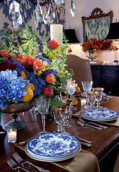 a dining room table set with blue and white plates, silverware and flowers in vases