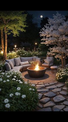 a fire pit in the middle of a garden at night with flowers and trees around it