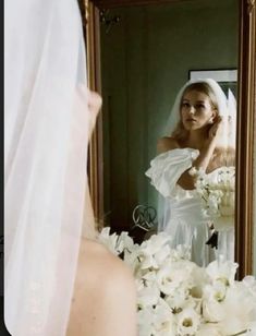 a woman in a wedding dress looking at herself in the mirror with flowers all around her