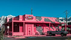 a truck parked in front of a pink building with mountains in the backgroud