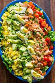 a blue plate topped with salad and meat on top of a wooden table next to a fork