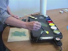 a man is painting on a table with paintbrushes