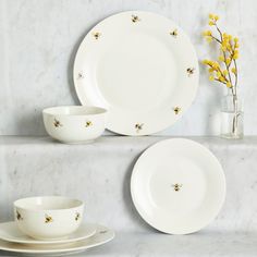 three plates and two cups on a shelf with flowers in vases next to them