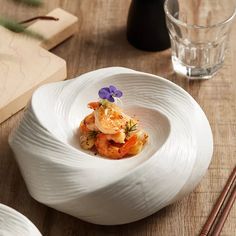 a white bowl filled with food next to chopsticks and a glass on a wooden table