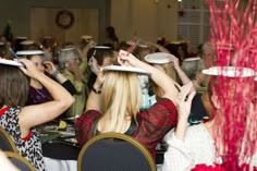 several people sitting at tables with paper plates on their heads and one person holding a cell phone up to her head