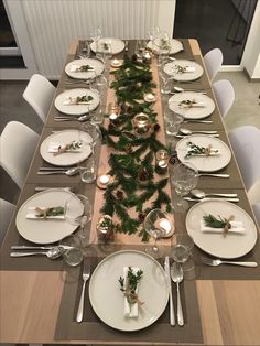 the table is set for christmas dinner with pine cones and greenery on it, along with silverware