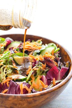 a wooden bowl filled with salad and dressing being poured onto it's side dish