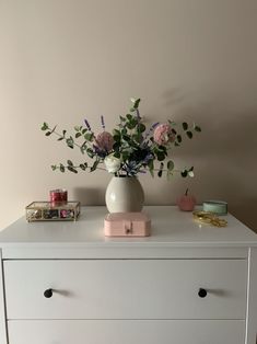 a vase with flowers on top of a white dresser next to other items and decorations