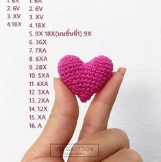 a hand holding a small crocheted pink heart in front of a white background