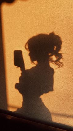 the shadow of a woman holding a cell phone in her hand and standing next to a wall