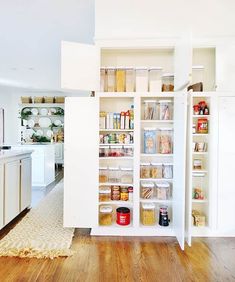 an organized pantry in the middle of a kitchen with white cabinets and wood flooring